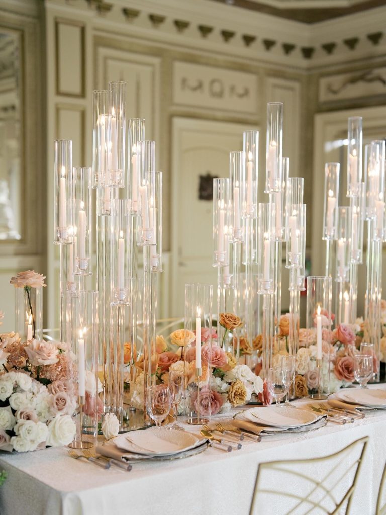 Elegant Columbus, Ohio wedding reception table featuring tall glass candleholders, glowing taper candles, blush pink and peach floral arrangements, ivory linens, gold flatware, and chic wedding rental décor.