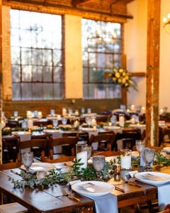 Rustic Reception with large windows and wooden tables with greenery and candle light