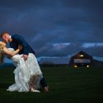 groom dipping his bride in an open field at night with a glowy dark blue sky