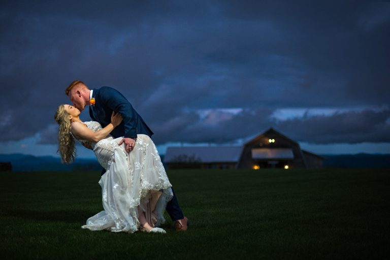 groom dipping his bride in an open field at night with a glowy dark blue sky