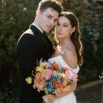 bride and groom taking outdoor wedding portraits after ceremony with color floral bouquet