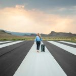 Woman traveling with suitcase walking on airplane runway