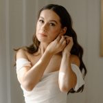 bride putting on earrings with natural wedding makeup and hollywood curls