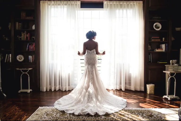 Bride looking out window showing back of wedding dress with train