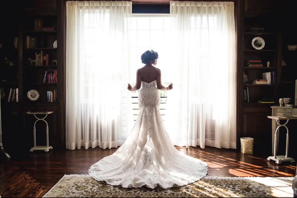 Bride looking out window showing back of wedding dress with train