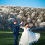 groom spinning his bride with trees and blue sky in the background