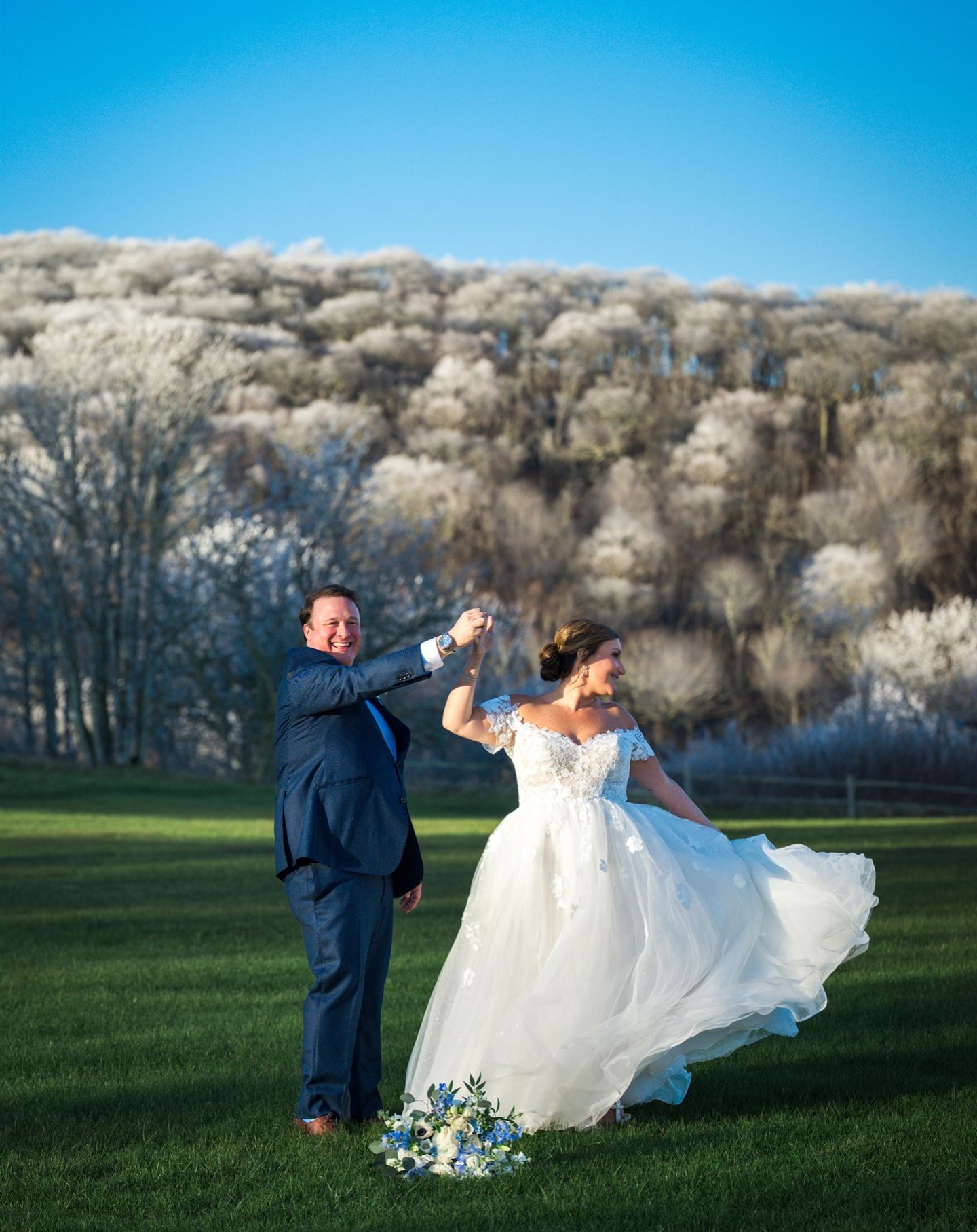 groom spinning his bride with trees and blue sky in the background