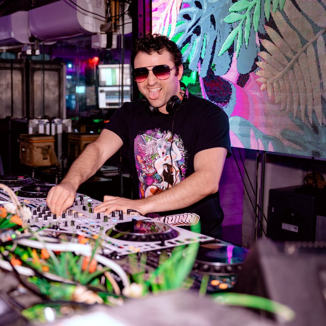 dj spinning dj board with colorful mural on wall behind him