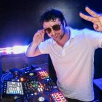 man dj at a wedding holding up a piece sign with sunglasses