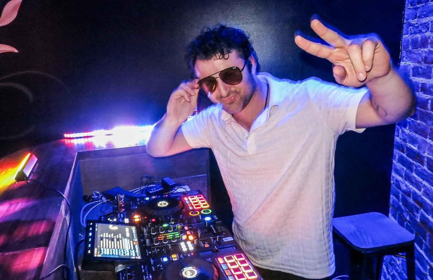 man dj at a wedding holding up a piece sign with sunglasses