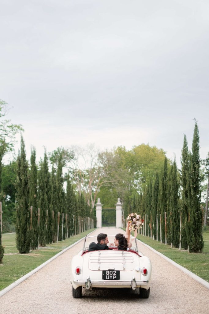 bride and groom in getaway car leaving venue surrounded by tall trees