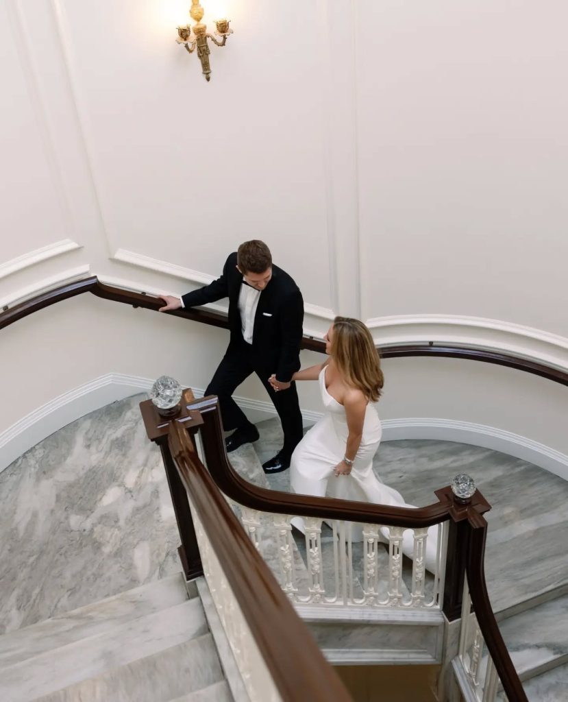 bride and groom walking up winding staircase at indoor luxury wedding reception