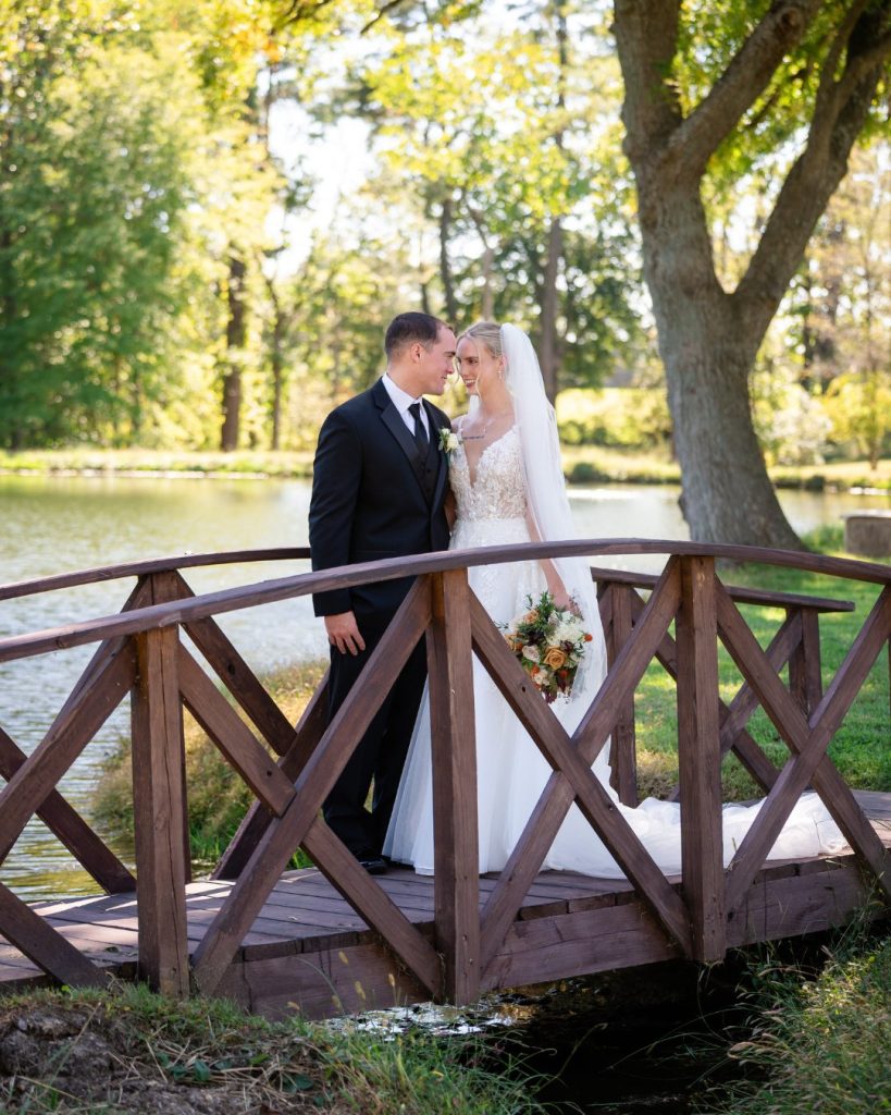 Bride and groom standing together on a wooden footbridge beside a pond at their fall wedding in Elkton, Maryland.