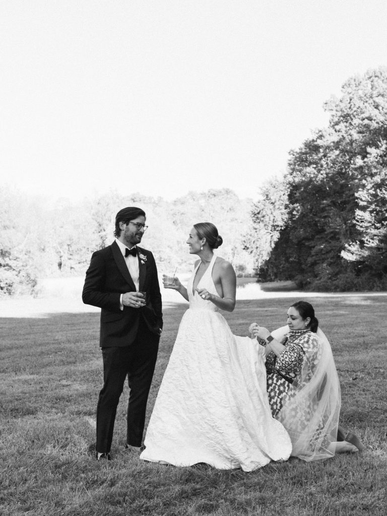 Wedding stylist adjusting a bride's gown and veil outdoors before portraits on the wedding day.