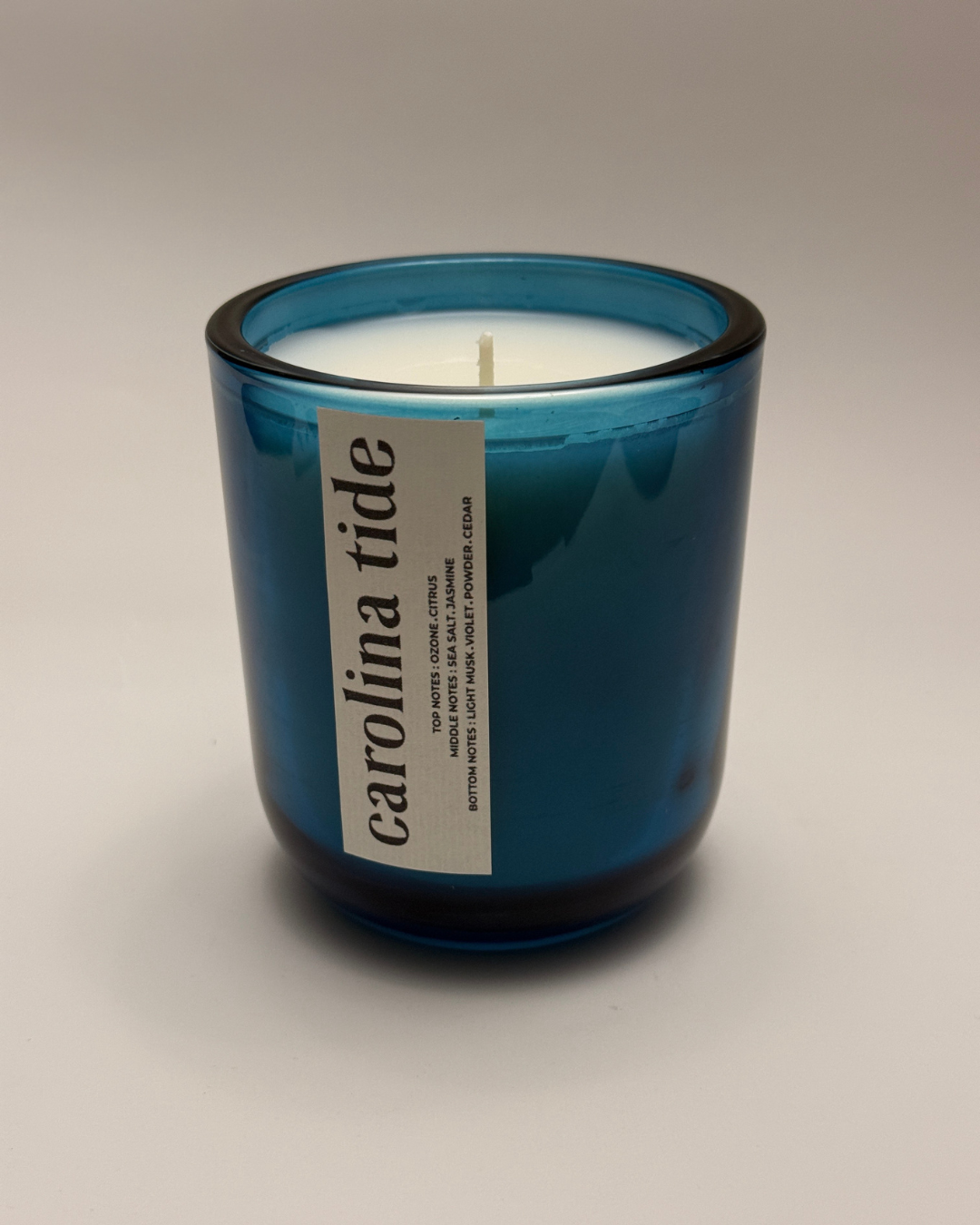 "Carolina Tide" candle in a deep cerulean blue glass jar with a white vertical label and scent profile.
