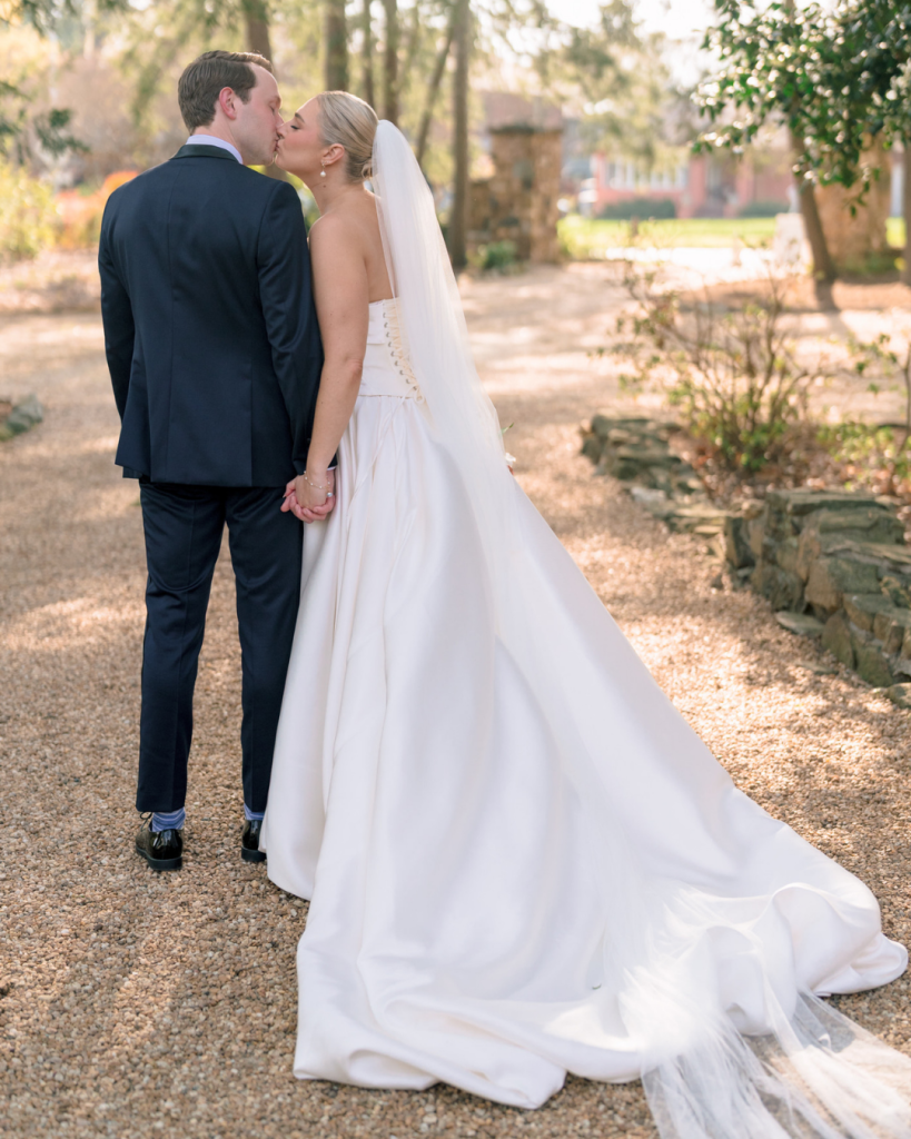 Bride and groom share a kiss while walking through the gardens at Van Landingham Estate after their spring wedding ceremony.
