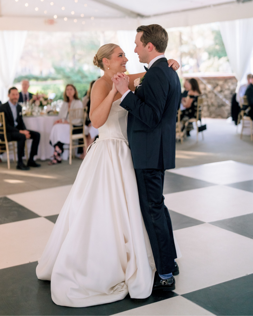Bride and groom share their first dance inside a white reception tent with black-and-white dance floor.