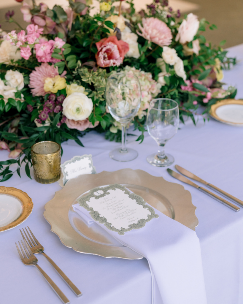 Romantic spring wedding tablescape with gold chargers, floral centerpiece, and elegant printed menu cards.