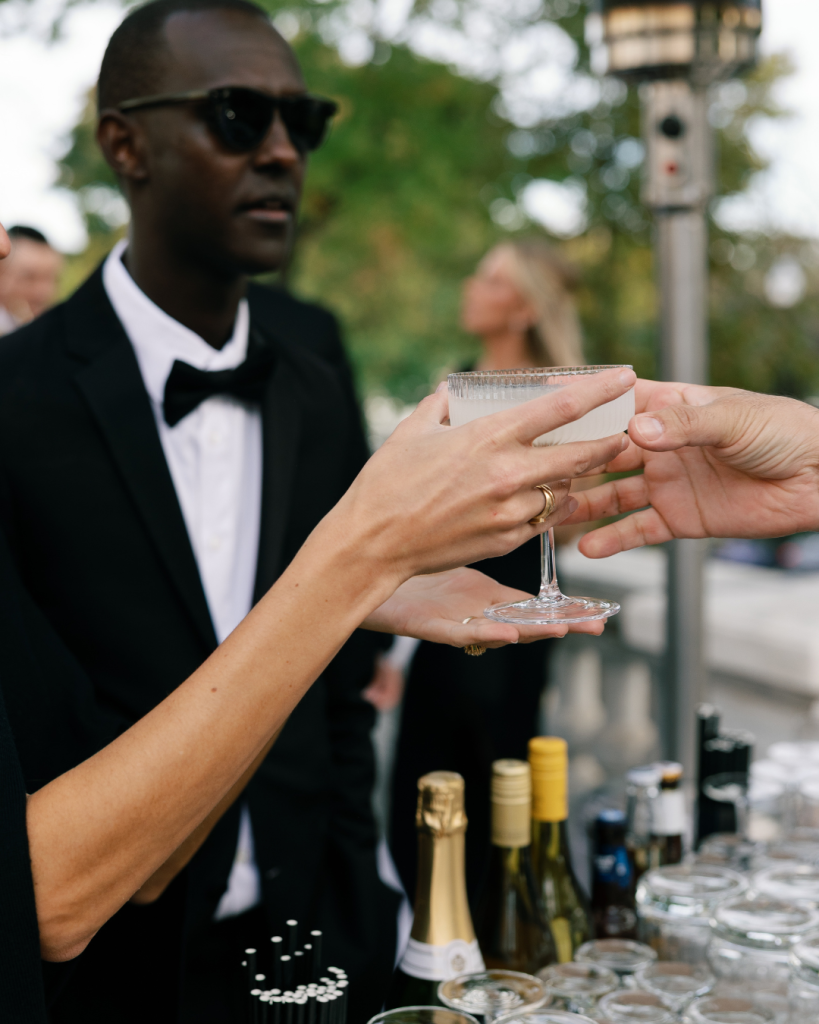 bartender passing signature cocktail to wedding guest at outdoor bar