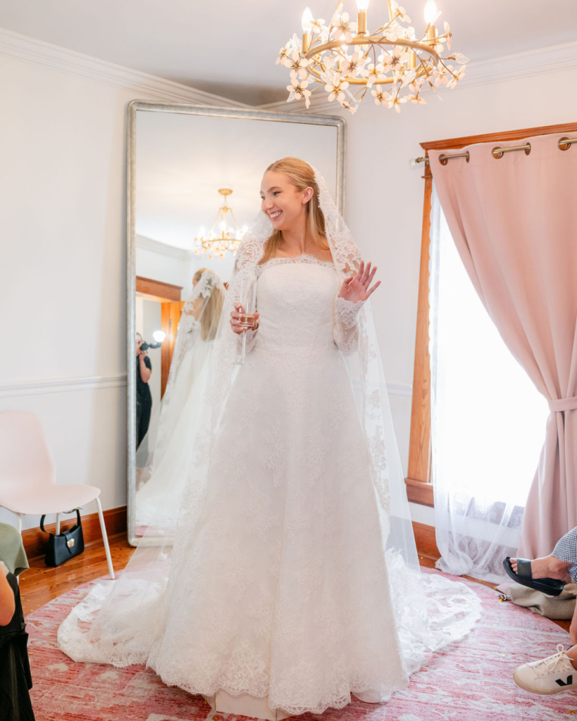 Bride wearing a lace wedding gown and veil while celebrating with champagne during a bridal appointment at Gilded Social.