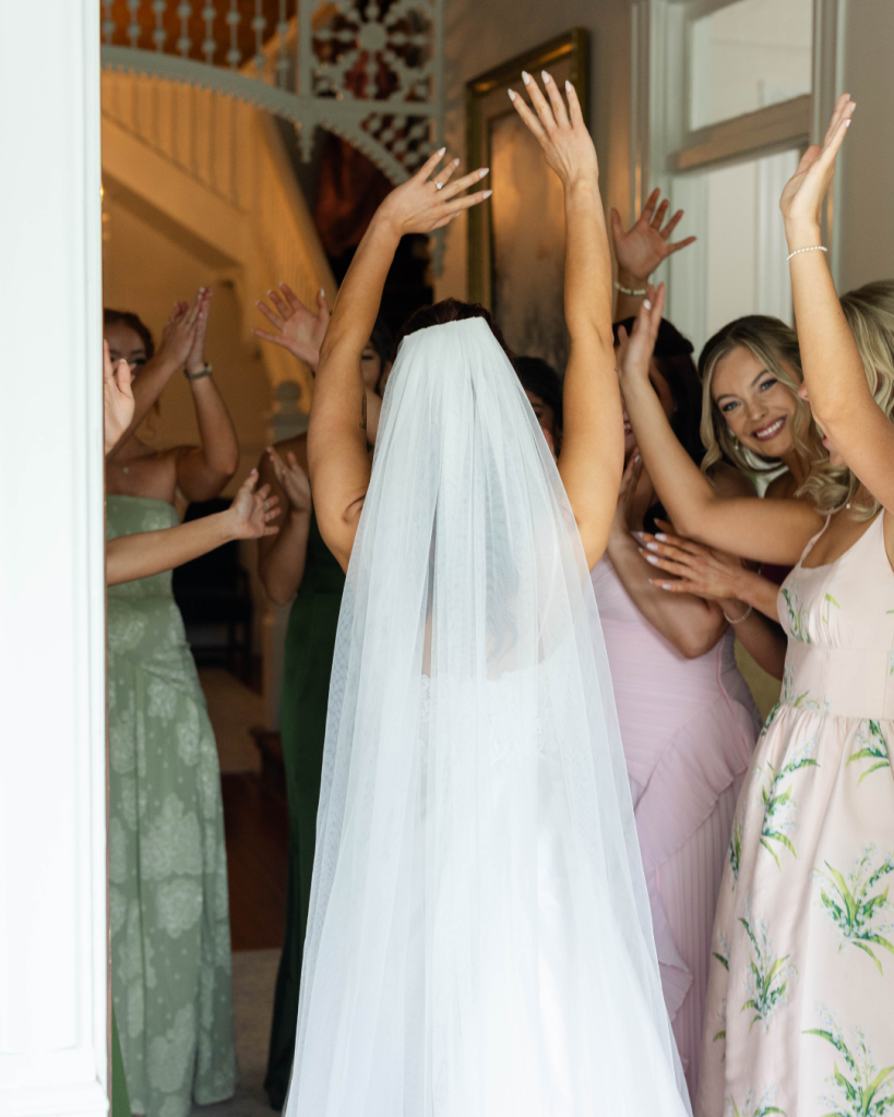 Bride entering the room with bridesmaids cheering during getting ready moments at a romantic Charlotte wedding featured by Wed Society Charlotte.