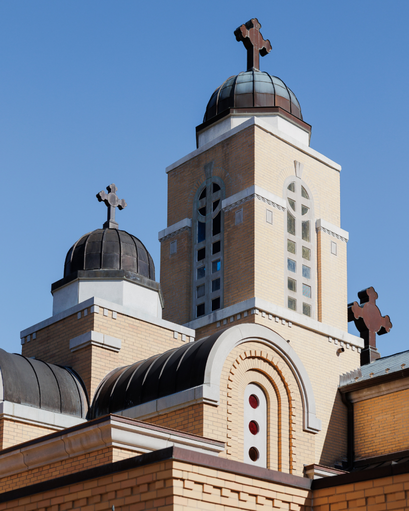 Exterior architecture of Holy Trinity Greek Orthodox Cathedral in Charlotte, North Carolina featuring iconic domes and crosses against a blue sky.