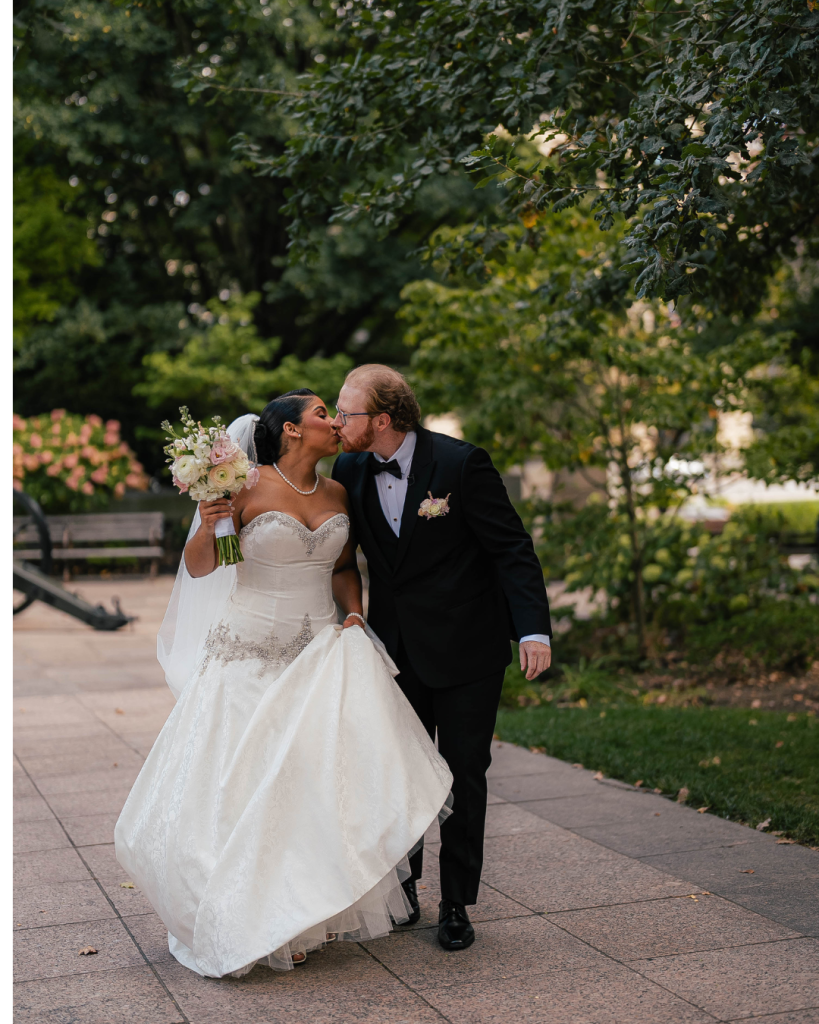 Newlywed couple kissing while walking outdoors during black tie wedding portraits surrounded by greenery in Columbus, Ohio.