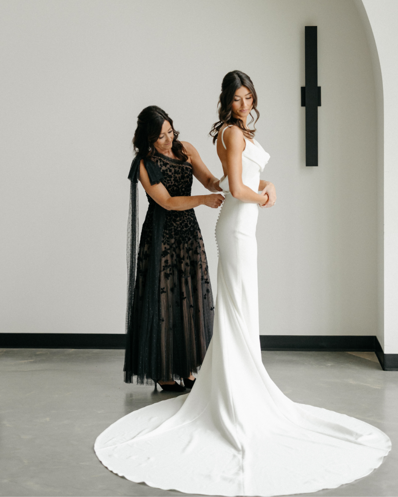 Bride getting ready in a minimalist fitted gown with long train inside a modern venue Ceremony space with wooden chairs and floor to ceiling windows at The Lumen House near Charlotte