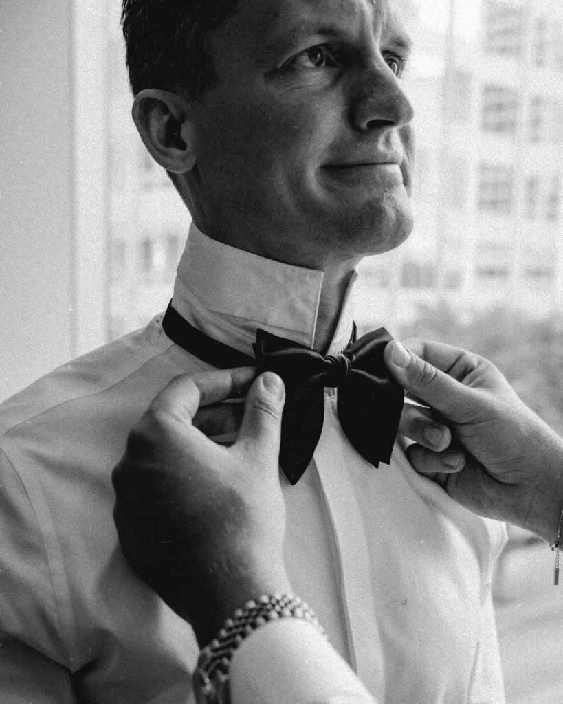 Close up black and white portrait of a groom having his bow tie adjusted before his Charlotte wedding at The Mint Museum.