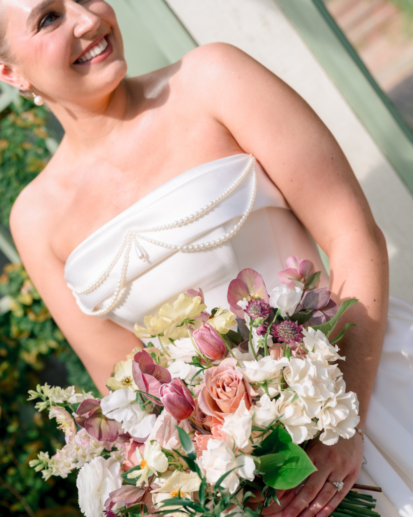 Close-up of bride’s pearl-detailed wedding gown and pastel spring bridal bouquet featuring blush, cream, and mauve blooms.