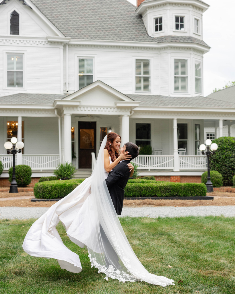 Bride and groom portrait outside The Grande Victorian featuring dramatic veil movement and elegant garden party wedding style.