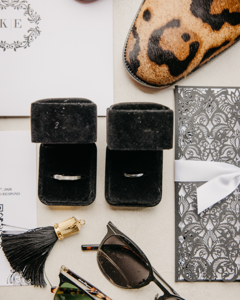 Wedding detail flat lay featuring wedding bands, invitation suite, accessories, and black and white design elements for a Charlotte wedding.