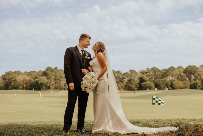 Full-length bride and groom portrait on golf course at Bayside Resort Golf Club under soft autumn sky