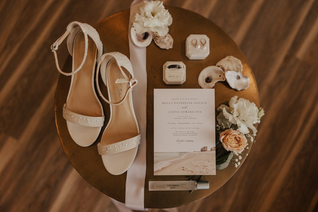 Coastal-inspired wedding invitation suite with bridal shoes, rings, oyster shells, and soft neutral details at Bayside Resort Golf Club