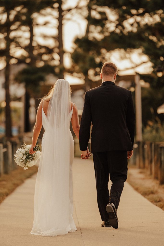 Bride and groom walking hand in hand along a pathway at Bayside Resort Golf Club in Selbyville, Delaware, during golden hour wedding portraits.