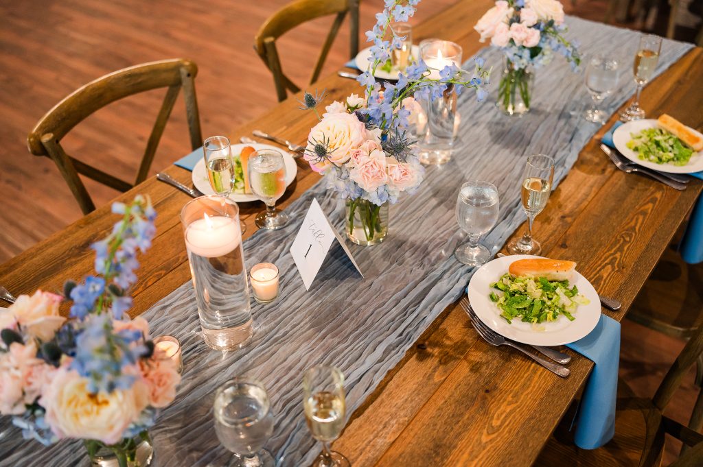 Reception table styling with blue floral centerpieces, candles, and wood farmhouse tables at King Cole Farm in Delaware.