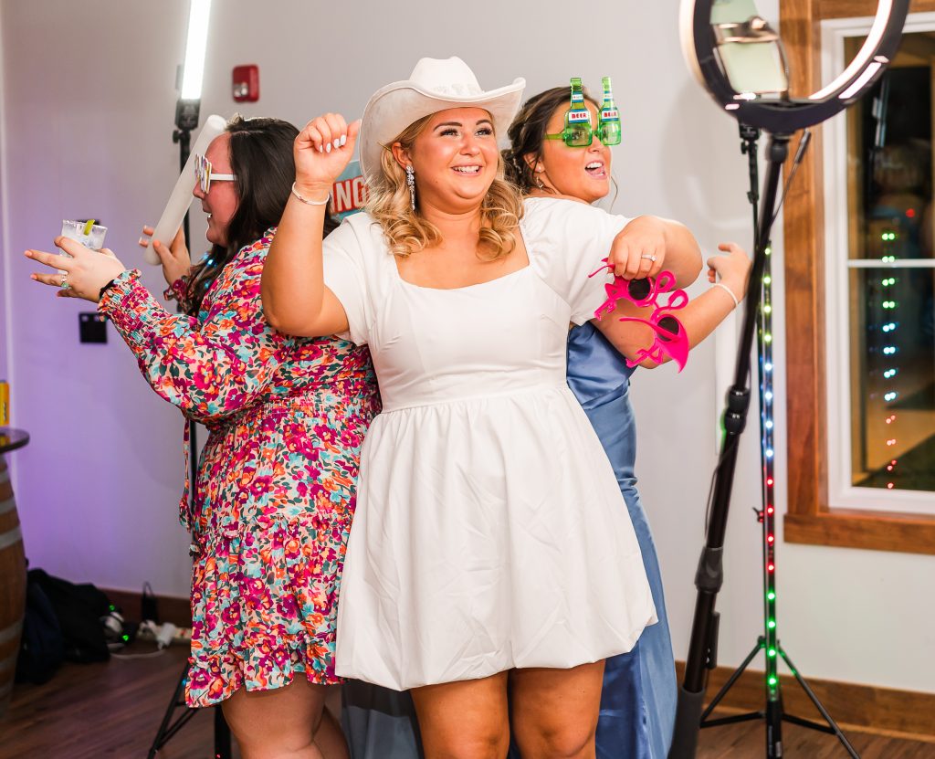 Bride dancing at the reception in a short white party dress, cowboy boots, and a white cowboy hat during the wedding celebration.