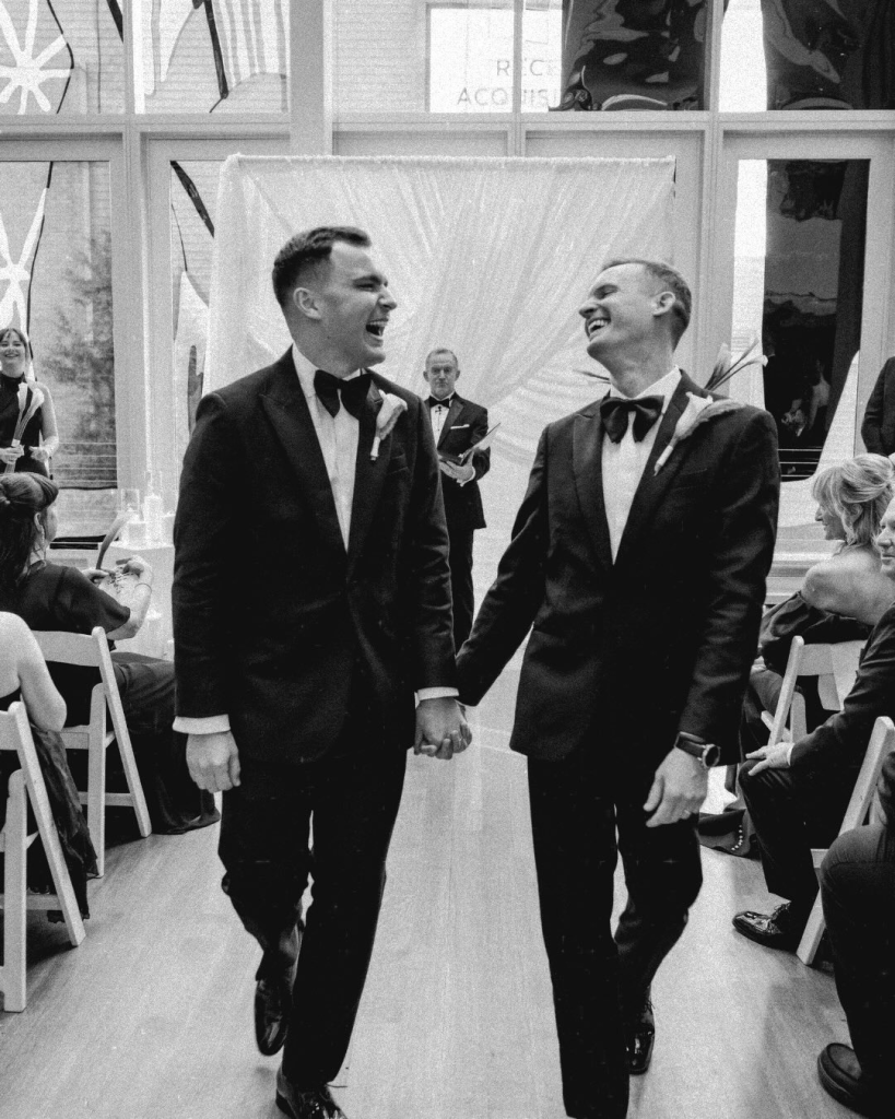 Eric and Kyle smile and walk hand in hand down the aisle during their joyful ceremony at The Mint Museum in Charlotte.
