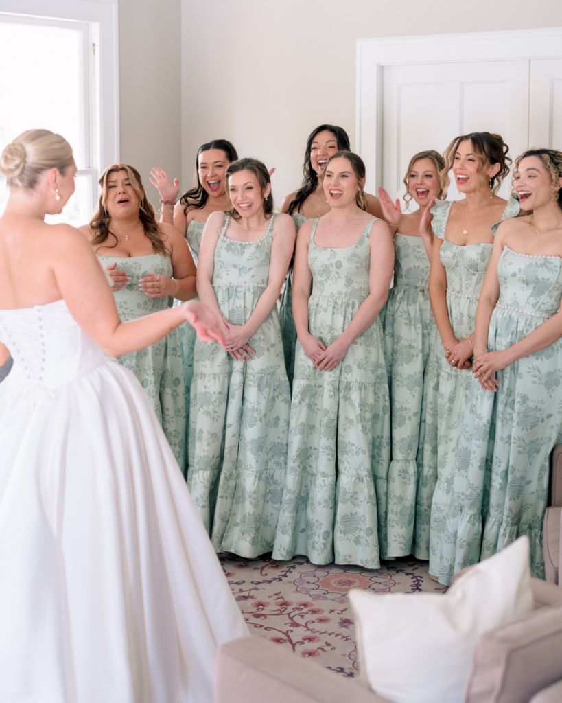 Bridesmaids react emotionally as bride reveals her wedding dress during bridal getting ready moments.
