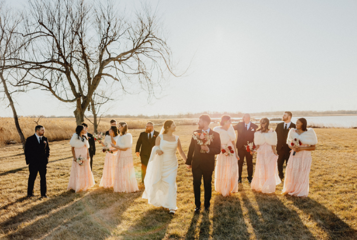 Bride and groom walking with wedding party through open field at Northern Delaware farm wedding during golden winter light
