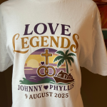 White tee with "Love Legends" graphic, wedding rings, a cross, and a cruise ship at sunset for Johnny and Phyllis.