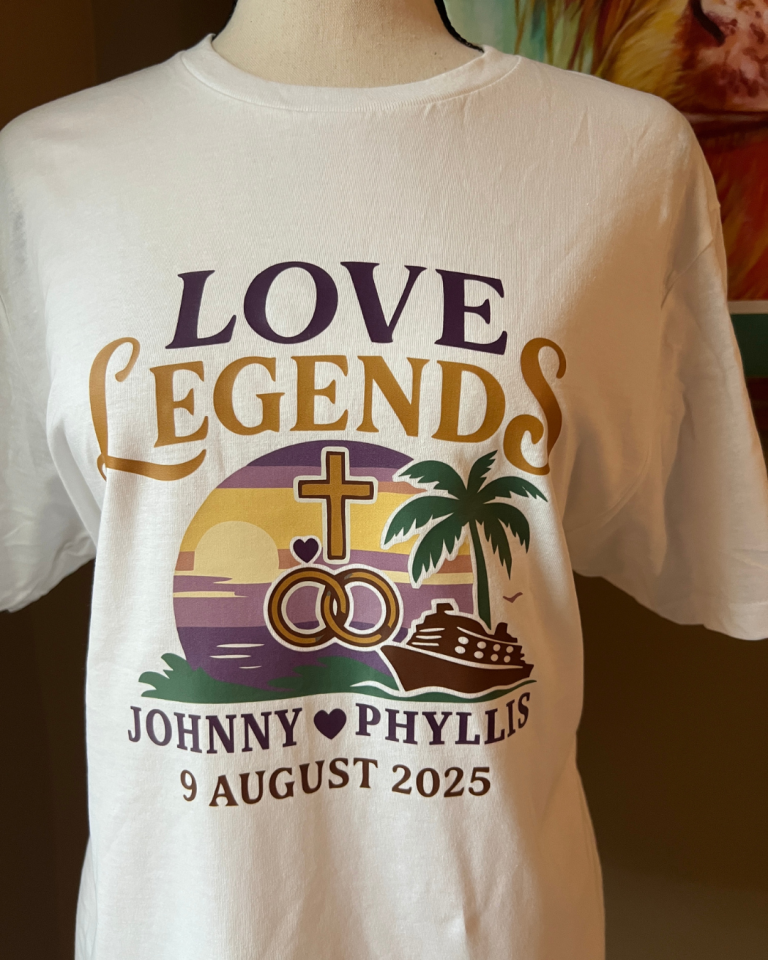White tee with "Love Legends" graphic, wedding rings, a cross, and a cruise ship at sunset for Johnny and Phyllis.