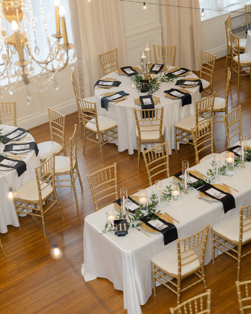 Elegant wedding reception tablescape with gold chiavari chairs, black napkins, candles, and greenery at The Hotel Concord.