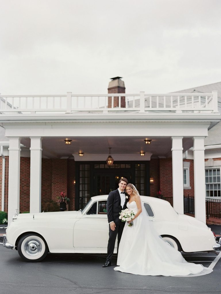 A bride and groom posing in front of their getaway car.