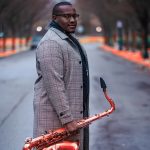 Anthony Saxson holding a saxophone on a city street.