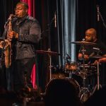 Anthony Saxson performing saxophone with a live band onstage.