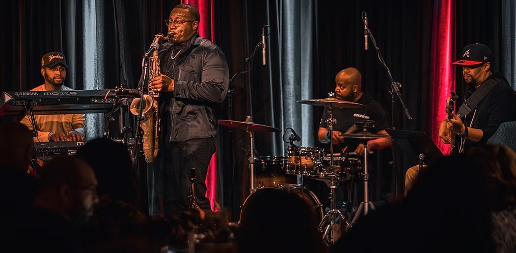 Anthony Saxson performing saxophone with a live band onstage.