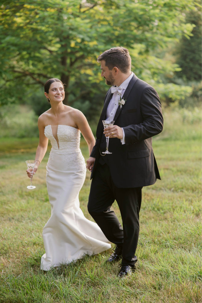 Bride and groom walking in the grass holding champagne glasses on a private estate near Columbus Ohio