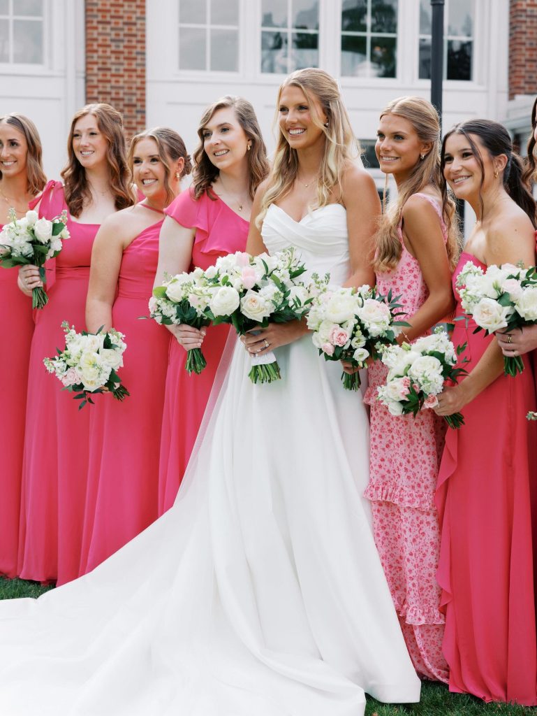 A bride surrounded by her bridesmaids in bright pink dresses.