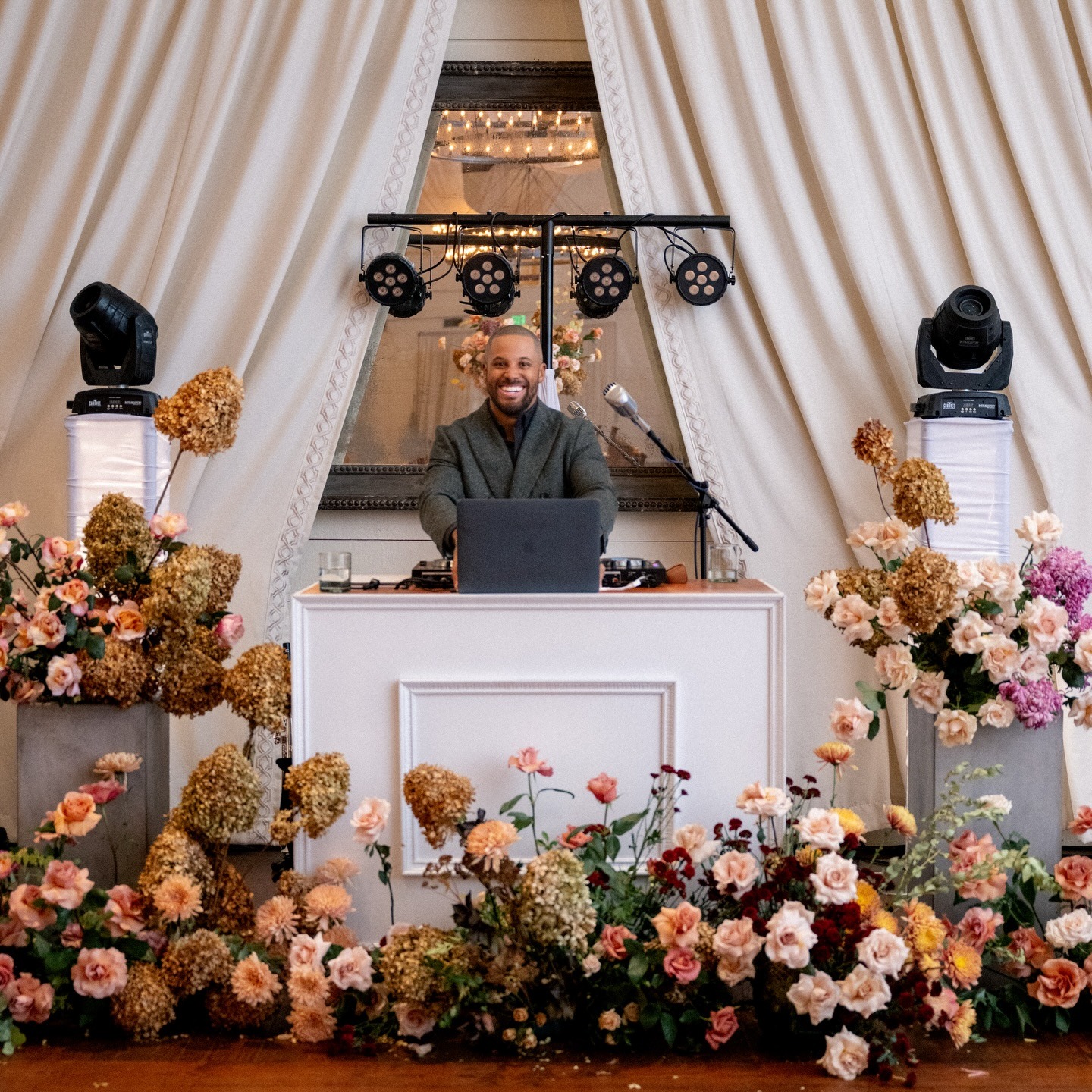 DJ standing behind music equipment with flowers all around his set up with white draping